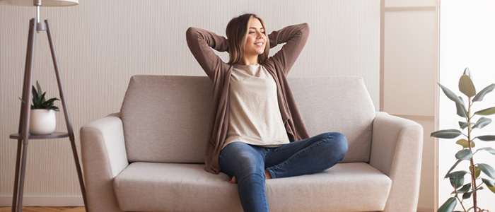 Mulher sentada em sofá, sorrindo e enquanto descansa.