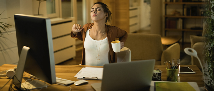 Mulher em home office, se espreguiçando.