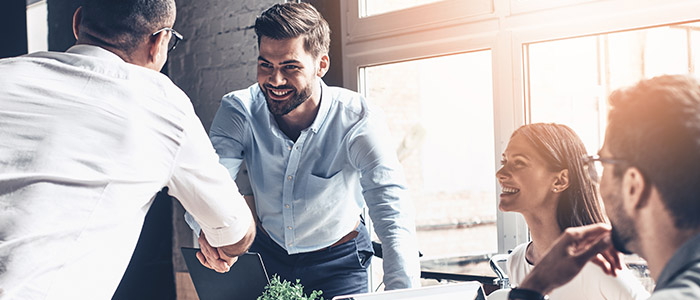 RH: Pessoas em escritório conversando, enquanto dois homens sorriem e apertam as mãos.